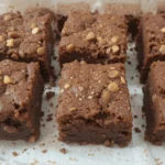 Square brownies with nuts on top, arranged on parchment paper.