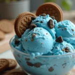 Bright blue ice cream with chocolate chip cookie pieces in a glass bowl, garnished with whole cookies.