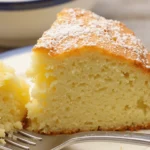 Slice of light-colored, moist cake dusted with powdered sugar on a blue and white plate with a fork